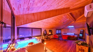 A cozy room with a wooden ceiling, a bathtub with candles, a red chair, and a small table with flowers.