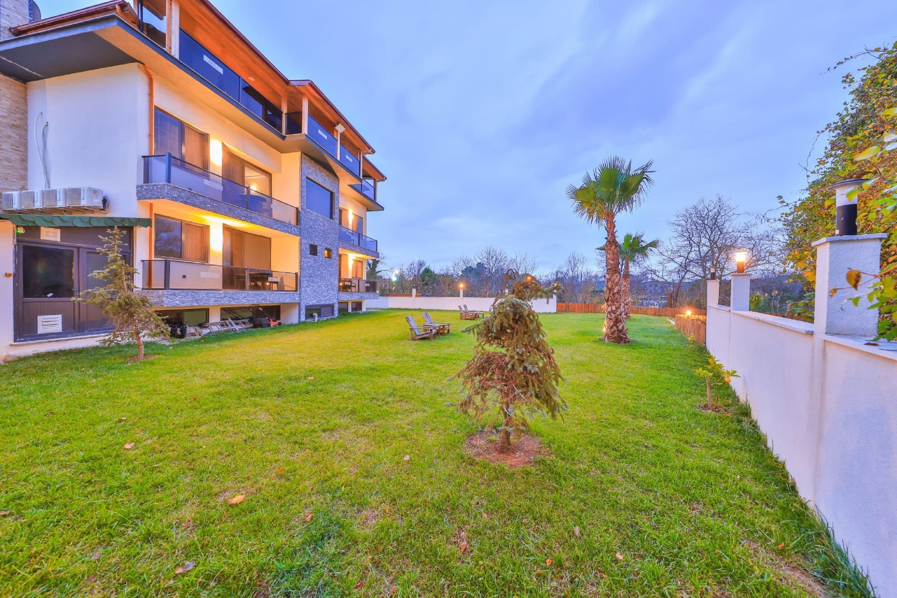 A modern multi-story building with balconies, a well-maintained lawn, and a few small trees.