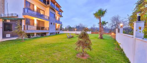 A modern multi-story building with balconies, a well-maintained lawn, and a few small trees.