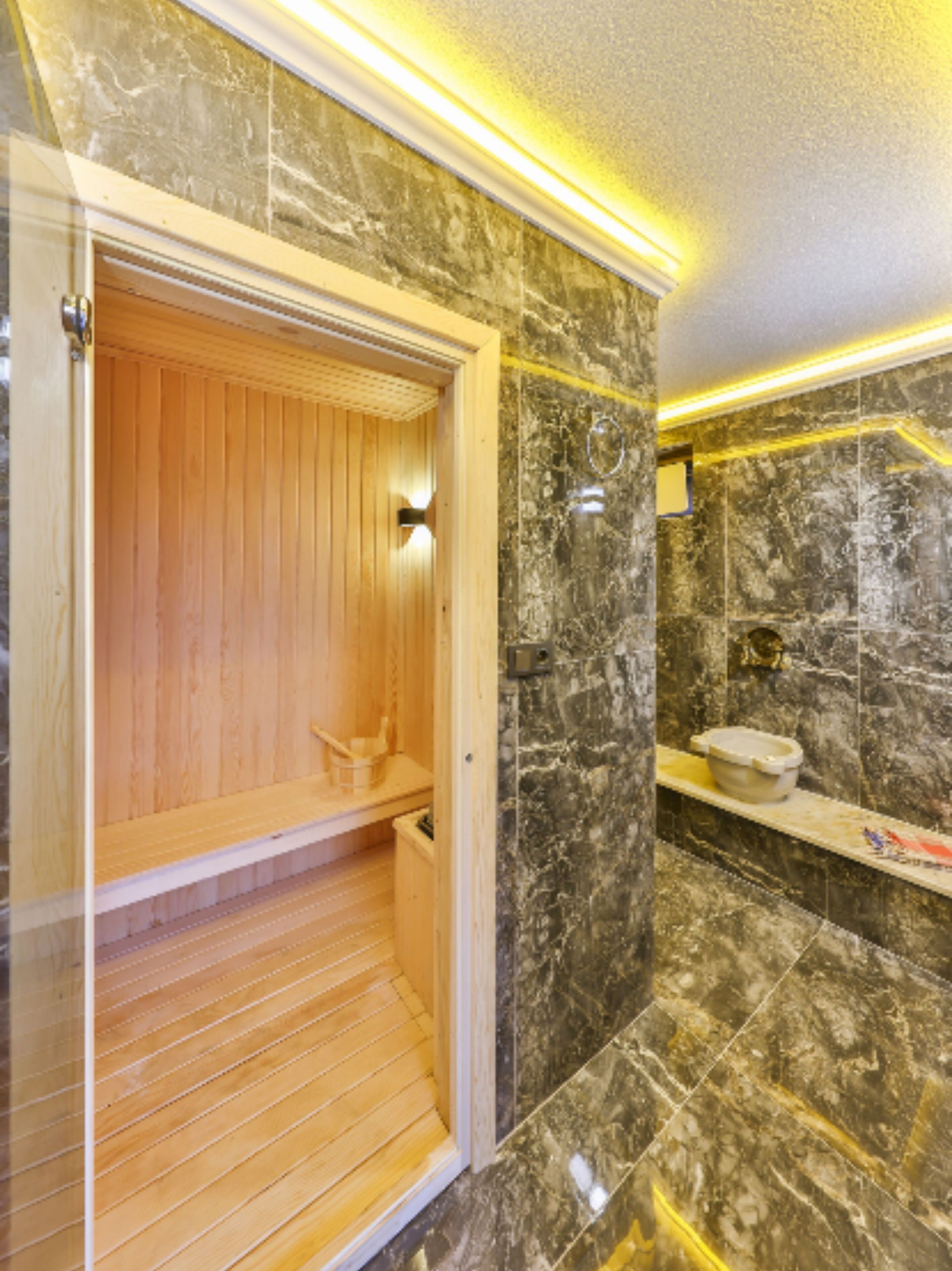 A sauna room with wooden benches, a marble-tiled wall, and a small shelf with a bowl.