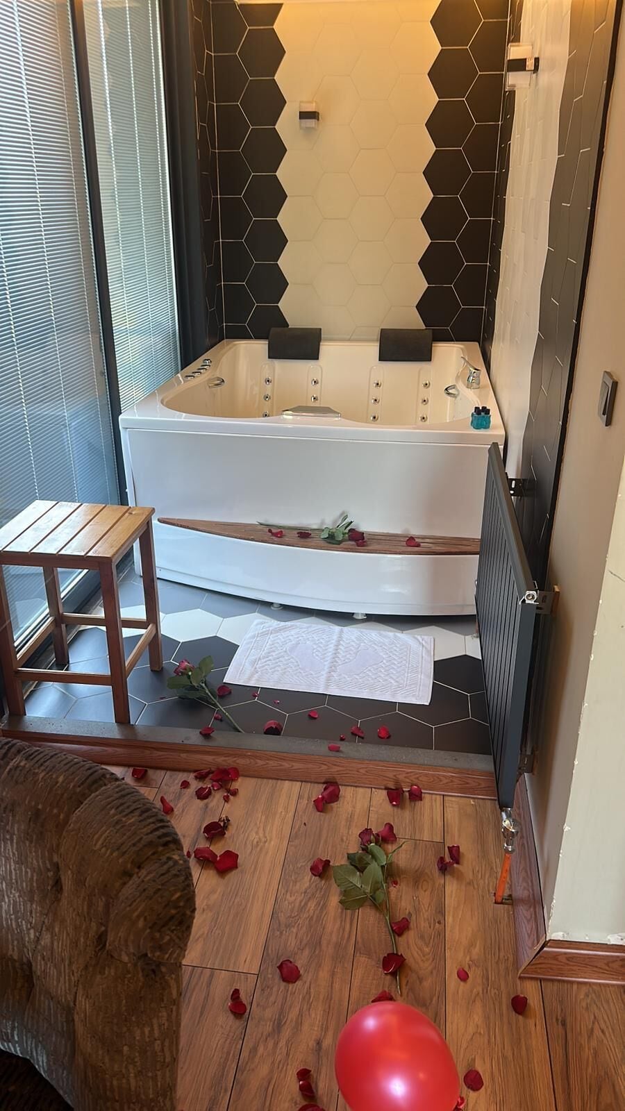 A bathroom with a bathtub, a wooden stool, rose petals, and a red balloon on the floor.