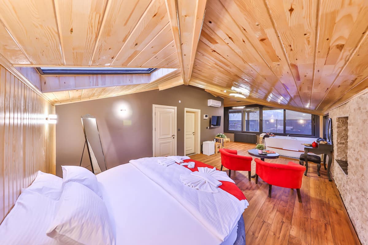 A hotel room with a wooden ceiling, a bed with white linens, a red sofa, and a small table.