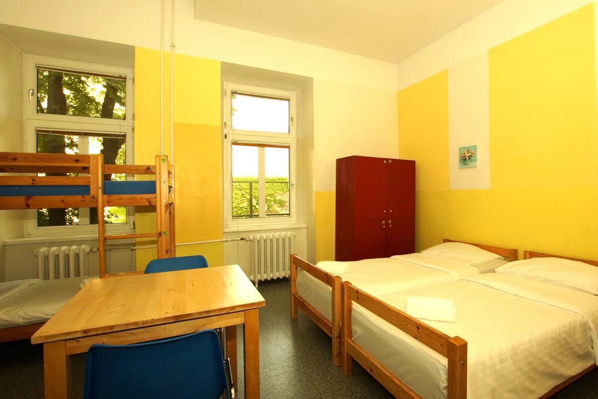 A dormitory room with bunk beds, a desk, a red wardrobe, and a bed.