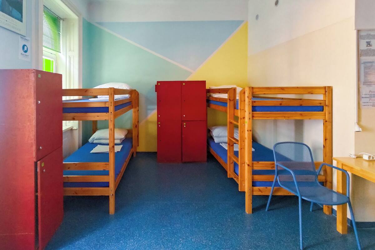 A dormitory room with bunk beds, a red wardrobe, a desk, and a chair.