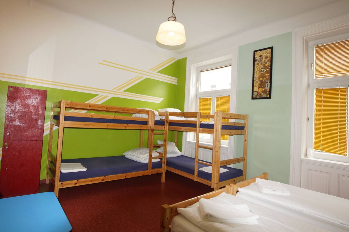 A room with bunk beds, a desk, and a window with blinds.