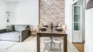 Un saló modern amb un sofà gris, una taula de dinar per a quatre persones i una paret amb relleu de maó.