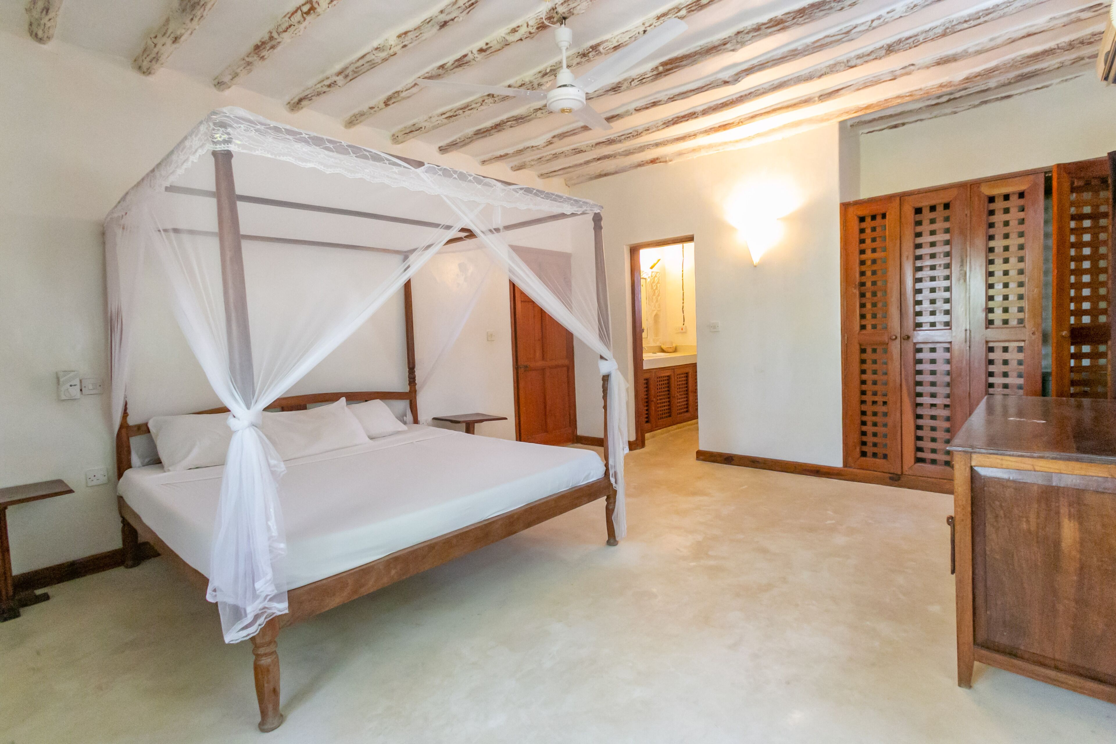 A bedroom with a four-poster bed, wooden wardrobe, and a ceiling fan.