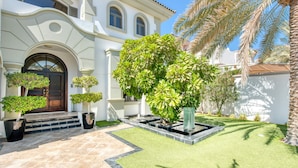 A white building with a large tree in the center, surrounded by smaller trees and a well-maintained lawn. - Maison Privee - Glamourous Beachfront Villa on The Palm w/ Pool (Dubai)
