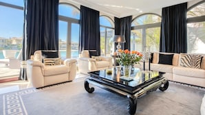 A spacious living room with a large glass coffee table, two sofas, and a view of a pool and buildings. - Maison Privee - Glamourous Beachfront Villa on The Palm w/ Pool (Dubai)