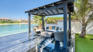 A covered outdoor seating area with a pool view, a pergola, and a palm tree. - Maison Privee - Glamourous Beachfront Villa on The Palm w/ Pool (Dubai)