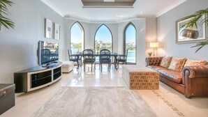 A spacious living area with a modern fireplace, a dining table with chairs, and a comfortable seating area with a sofa and ottoman. - Maison Privee - Glamourous Beachfront Villa on The Palm w/ Pool (Dubai)