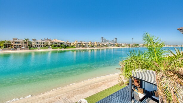 A beachfront property with a pool, outdoor seating, and a view of the sea and buildings in the background. - Maison Privee - Glamourous Beachfront Villa on The Palm w/ Pool (Dubai)