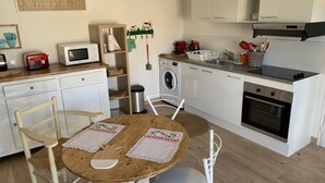 Cuina compacta amb microones, torradora i un rentaplat. Hi ha una taula de fusta amb dues cadires i un penjall decoratiu a la paret.