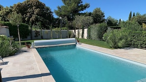 Una piscina rectangular amb aigua cristal·lina blava, envoltada per un solàrium amb rajoles i vistes a plantes i arbres.