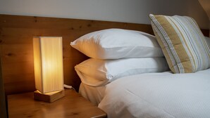 Un lit bien fait, avec du linge de lit blanc et un coussin à rayures, une table de chevet avec une lampe et une tête de lit en bois.