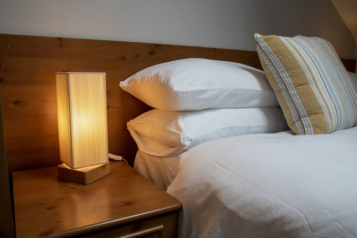 Un lit bien fait, avec du linge de lit blanc et un coussin à rayures, une table de chevet avec une lampe et une tête de lit en bois.