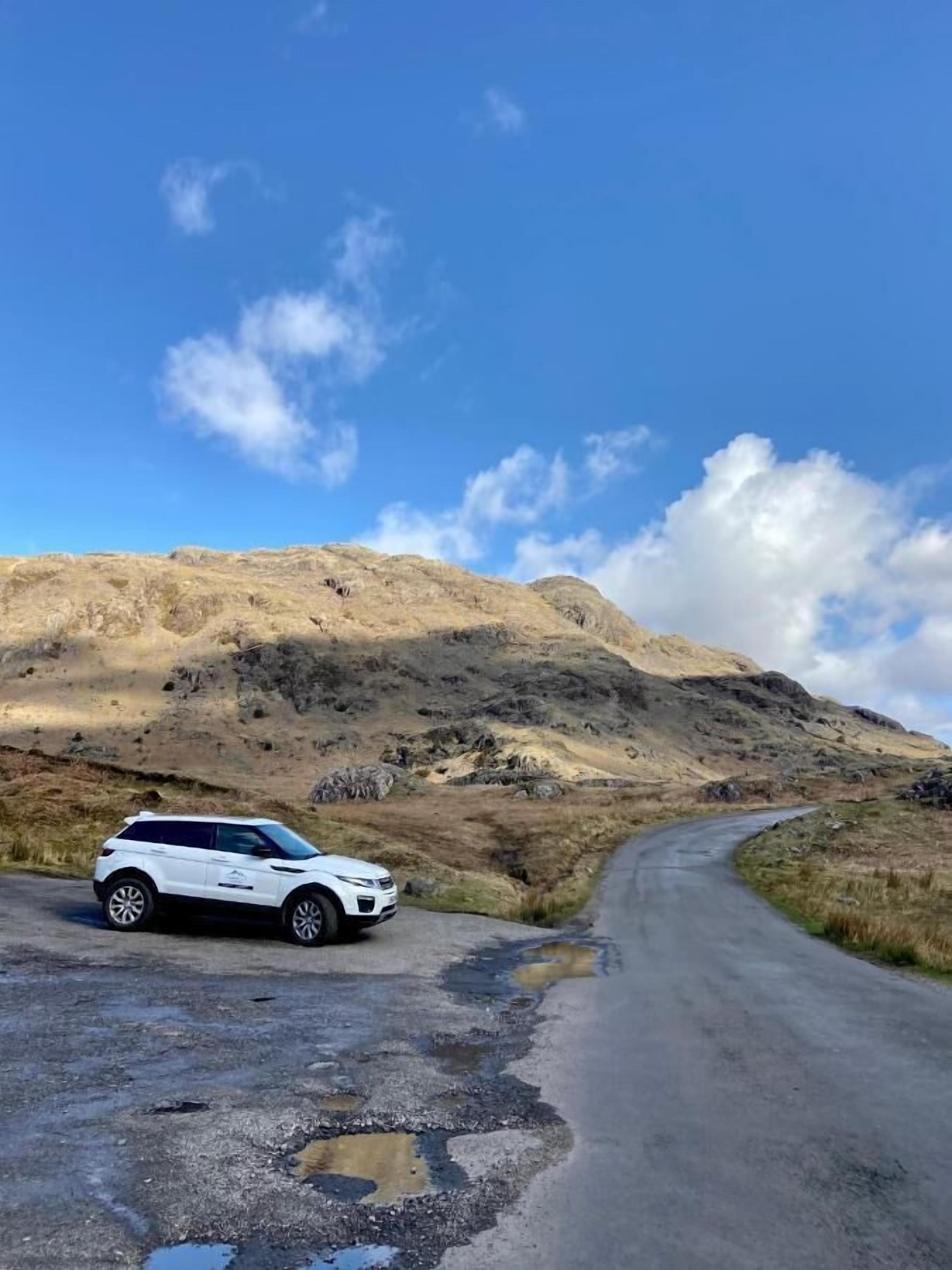 Un SUV blanco estacionado en una carretera sinuosa con montañas al fondo.