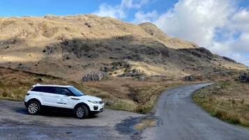 Un SUV blanco estacionado en una carretera sinuosa con montañas al fondo.