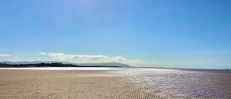 Una playa extensa de arena clara, cielo despejado y montañas a lo lejos.