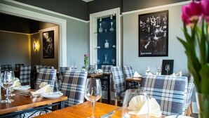 Un espace repas avec des banquettes à carreaux, des tables en bois et une étagère bleue où sont exposés des verres.