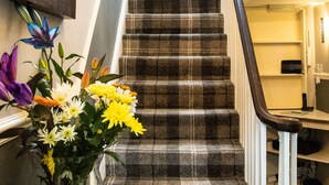 Un escalier recouvert d’une moquette à carreaux, un vase en verre rempli de fleurs et un lustre.