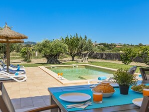 A poolside dining area with a table set for two, a bowl of bread, a glass of drink, and a plate of grapes. - Villa Can Segue · Villa with private pool in Alcúdia (Alcúdia)