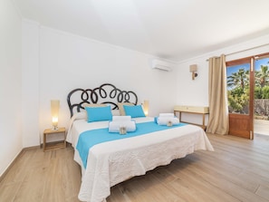 Una camera da letto con un letto, comodini, tende e vista su palme.