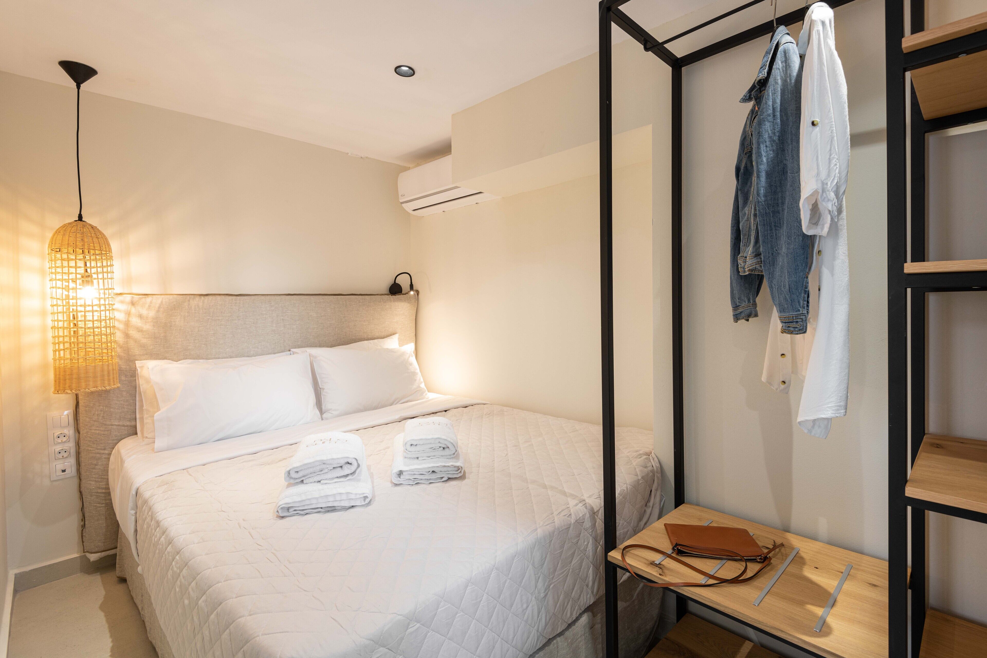 A neatly made bed with white linens and towels, a hanging light fixture, and a wooden bench with a bag and a book.
