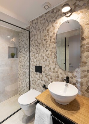 Une salle de bain moderne avec un mur décoré d’une mosaïque en pierre, un meuble-lavabo en bois, un lavabo blanc et des toilettes.