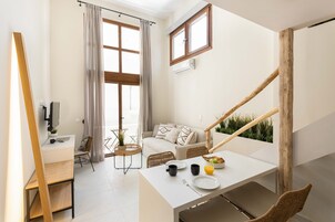 A modern, well-lit room with a dining table set for breakfast, a sofa, and a staircase with wooden railings.