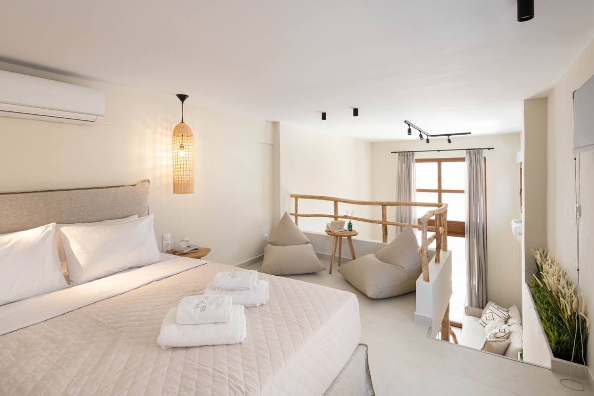 Una habitación de hotel moderna con una cama grande, una pequeña zona de estar y vistas al exterior.