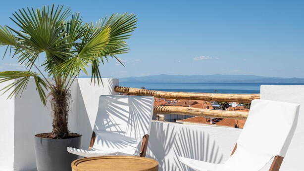 A terrace with a white chair, a small wooden table, and a potted plant. - Palm Residences (Kassandra)