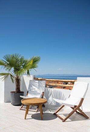 Une terrasse avec une chaise blanche, une petite table en bois et une plante en pot.