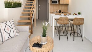 A modern apartment with a loft-style kitchen, a dining area with wicker chairs, a round coffee table, and a staircase leading to an upper level. - Palm Residences (Kassandra)