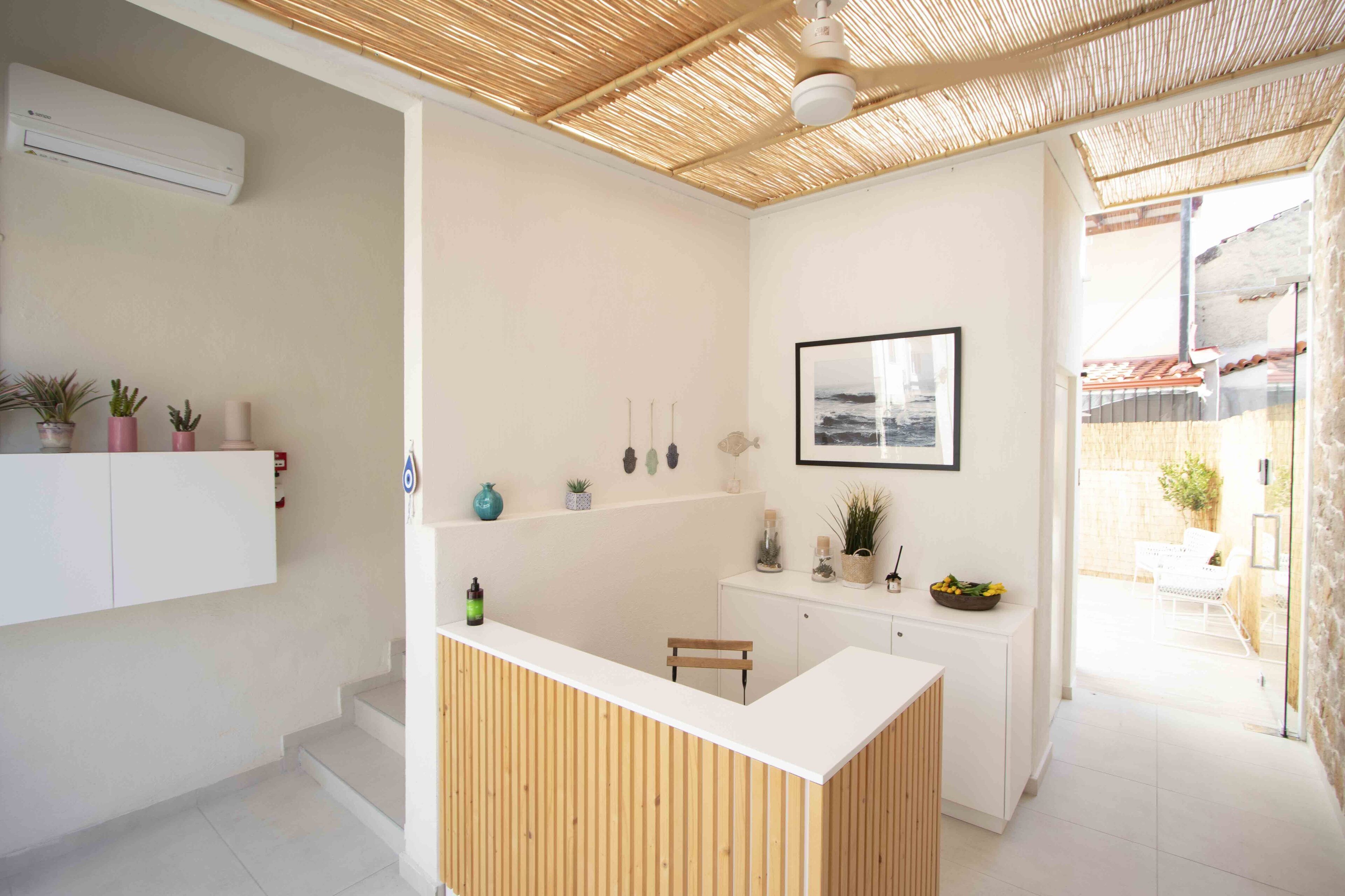 A modern reception area with a wooden reception desk, white walls, and a ceiling with a natural fiber texture. There are potted plants on a shelf and a framed picture on the wall.
