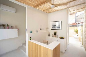 Un espace d’accueil moderne avec un comptoir de réception en bois, des murs blancs et un plafond à la texture naturelle. On y trouve des plantes en pot sur une étagère et un tableau encadré au mur.
