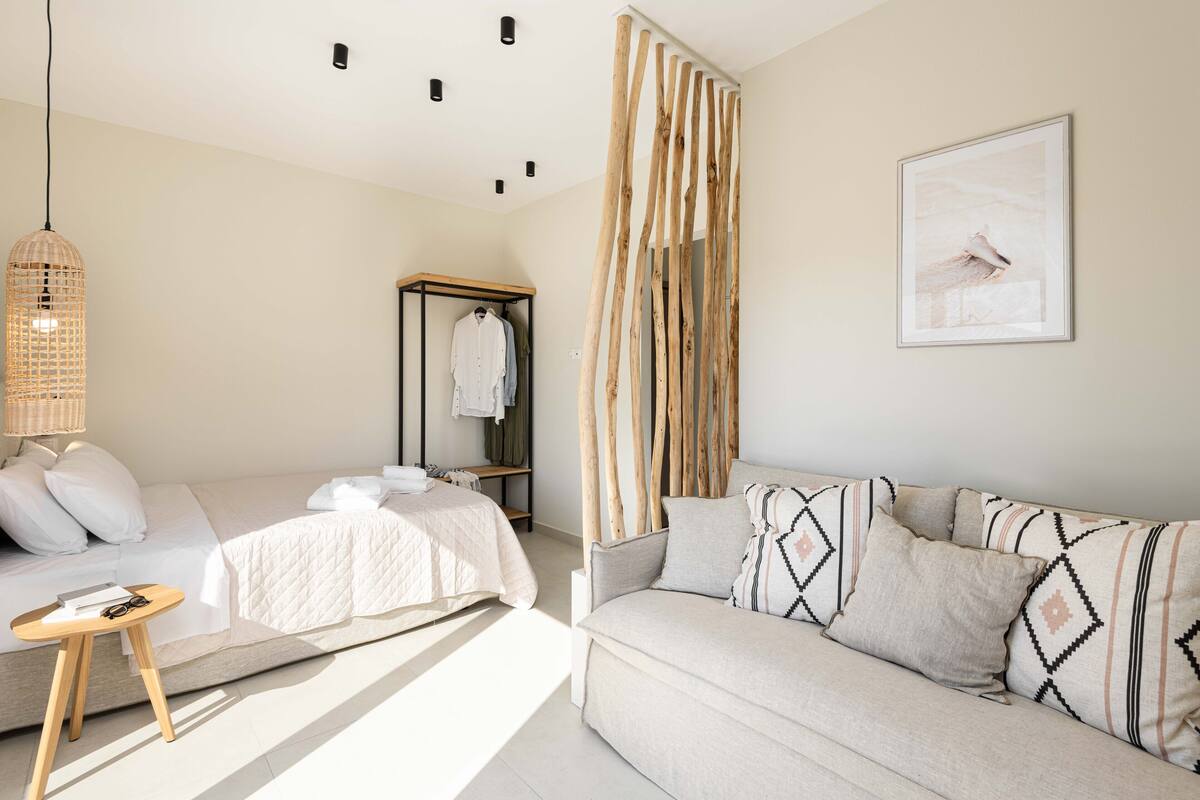 Una habitación de hotel moderna con una cama, un sofá, una lámpara colgante, un armario y un cuadro en la pared.