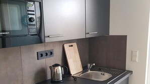 A modern kitchen with a built-in microwave, a kettle, a wooden cutting board, and a dishwasher. - Boardinghouse am Borkumkai (Emden)