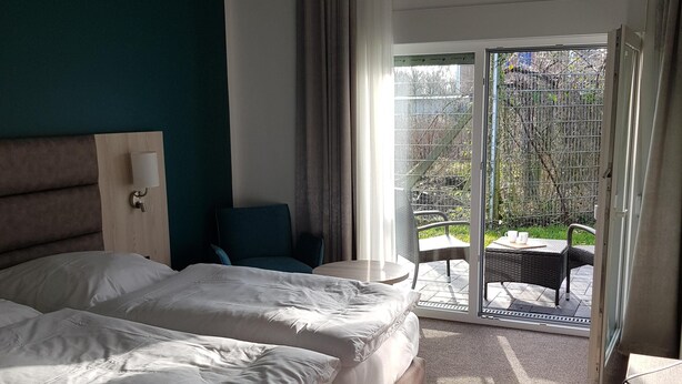 A hotel room with a large bed, a desk, a chair, and a view of the outdoor area through a sliding door. - Boardinghouse am Borkumkai (Emden)