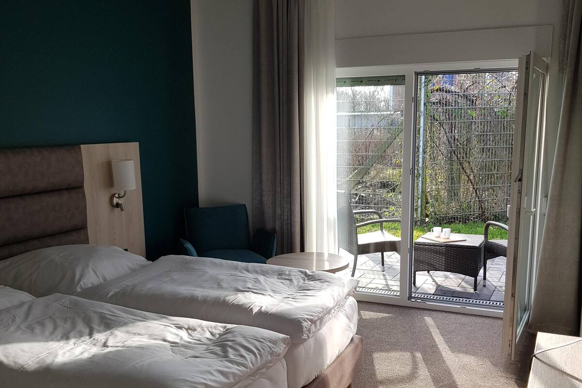 A hotel room with a large bed, a desk, a chair, and a view of the outdoor area through a sliding door.