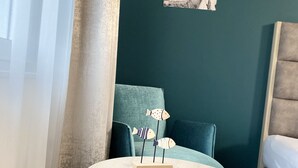 A round wooden table with three fish-shaped decorations, a teal sofa, and a bed in a room with teal walls and a framed picture. - Boardinghouse am Borkumkai (Emden)