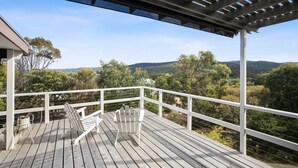 Una terraza de madera con barandas blancas y sillas Adirondack, con vistas a un paisaje montañoso.