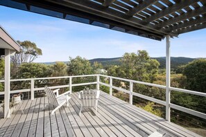 Eine Holzterrasse mit weißen Geländern und Adirondack-Stühlen mit Blick auf eine hügelige Landschaft.