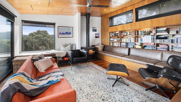 Una sala de estar moderna con chimenea, sofás de cuero, una estantería y un ventanal con vistas al exterior.