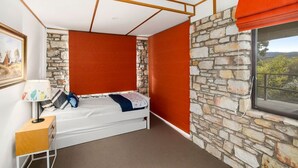 Un dormitorio con cama, mesita de noche, lámpara, ventana con vistas y pared de piedra.