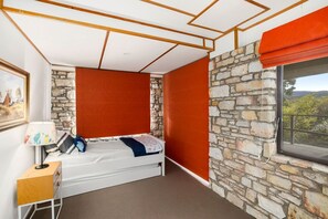 Ein Schlafzimmer mit einem Bett, einem Nachttisch, einer Lampe, einem Fenster mit Blick und einer Steinwand.