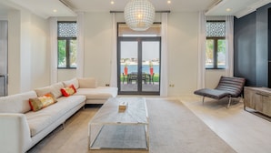 A modern living room with a sofa, a lounge chair, a coffee table, and a view through a glass door to an outdoor patio. - Maison Privee - Prvt Pool & Beach in Luxury Palm Jumeirah Villa (Dubai)