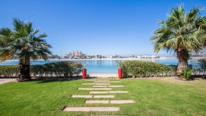 A pathway leading to a beach with palm trees and a view of a coastal cityscape. - Maison Privee - Prvt Pool & Beach in Luxury Palm Jumeirah Villa (Dubai)