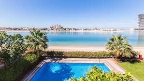 A pool area with a view of the beach and distant buildings. - Maison Privee - Prvt Pool & Beach in Luxury Palm Jumeirah Villa (Dubai)