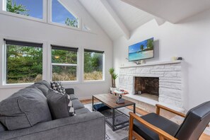 A modern living room with a fireplace, large windows, and a TV mounted above it.